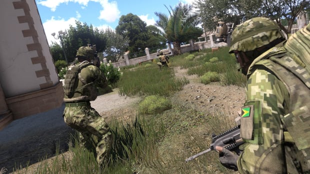 Three soldiers in Arma 3 - two close to the camera and one further out. There's a building on the left of the image and there are trees in the distance.