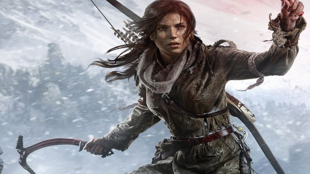 Phoebe Waller-Bridge is writing a new Tomb Raider Amazon series: A white woman with long brown hair, wearing a ragged grey snowsuit, is standing in the middle of a snowstorm. In her right hand is a rock climbing tool, while her left hand is raised in warning, and a bow is on her back
