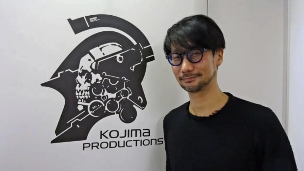 Hideo Kojima stands in front of his company logo and smiles seductively at the camera.