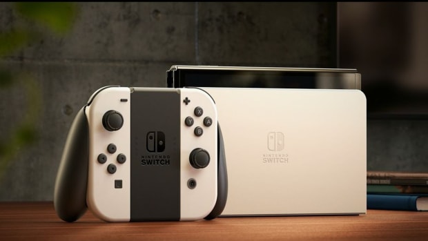 A white Nintendo Switch OLED model sitting in its dock, with Joy-Con controllers to its left