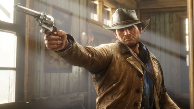 Red Dead Redemption 2's Arthur Morgan standing in a ramshackle wooden building with sunlight pouring in through the cracks, pointing a gun at someone off-screen