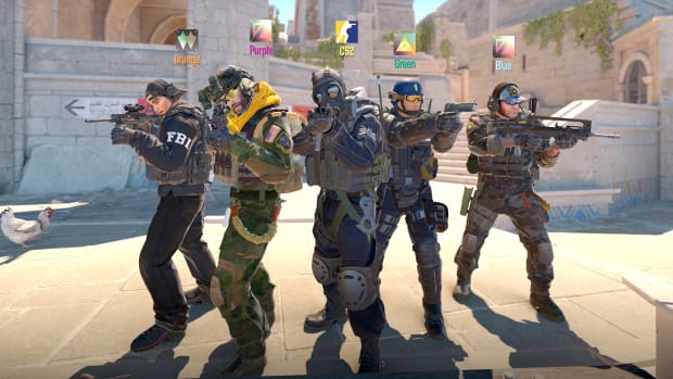 Five men wearing camo, helmets, and body armor stand in a loose V-shape in the middle of a paved plaza, pointing guns ahead of themselves