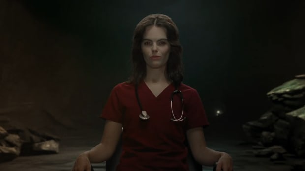 Diablo 4 Blood Harvest promo trailer screenshot of a vampiric looking doctor sitting on a chair.