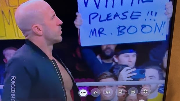 Photo of a TV screen showing someone hold up a sign at a wrestling event.