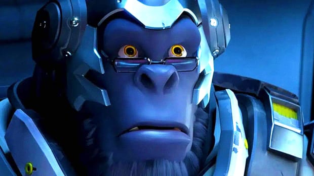 Overwatch 2's Winston is sitting in a dark room with a lit computer screen illuminating his bemused face
