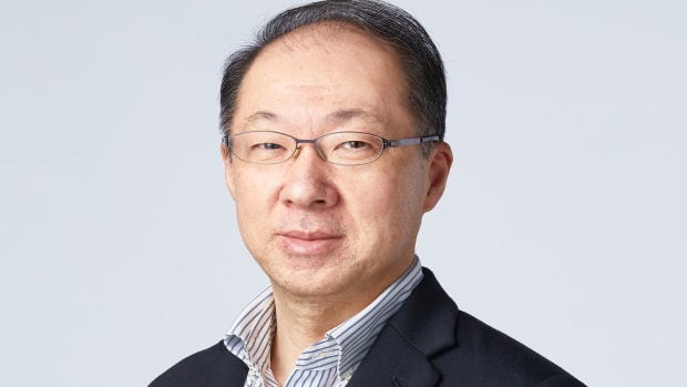 Nintendo composer Koji Kondo is shown, wearing rimless rectangular glasses and a dark navy suit jacket with a pinstriped, collared shirt
