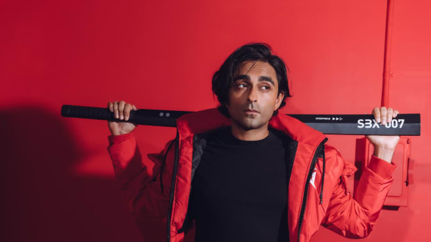 Adi Shankar holding a sword-like weapon in front of a red background