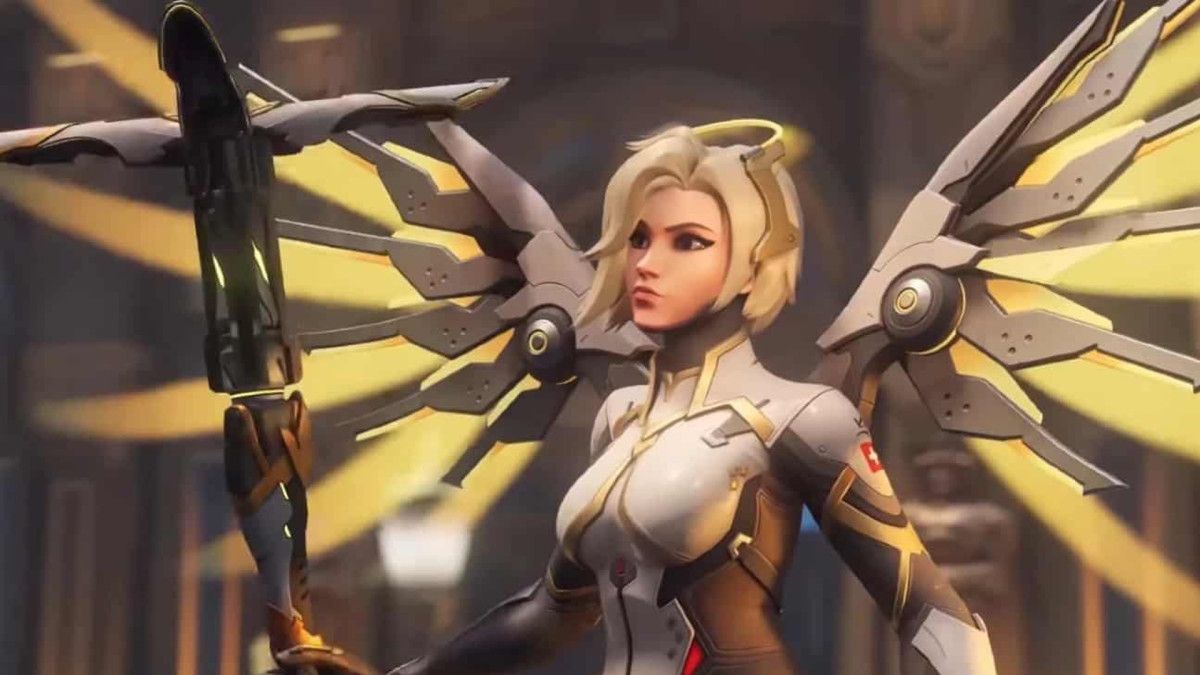 Overwatch 2 fans are clamoring for Mercy nerfs in the next update: A blonde woman in white metal armor, with yellow metal wings, is looking to her right with a serious expression. In her hands is a large caduceus-style staff
