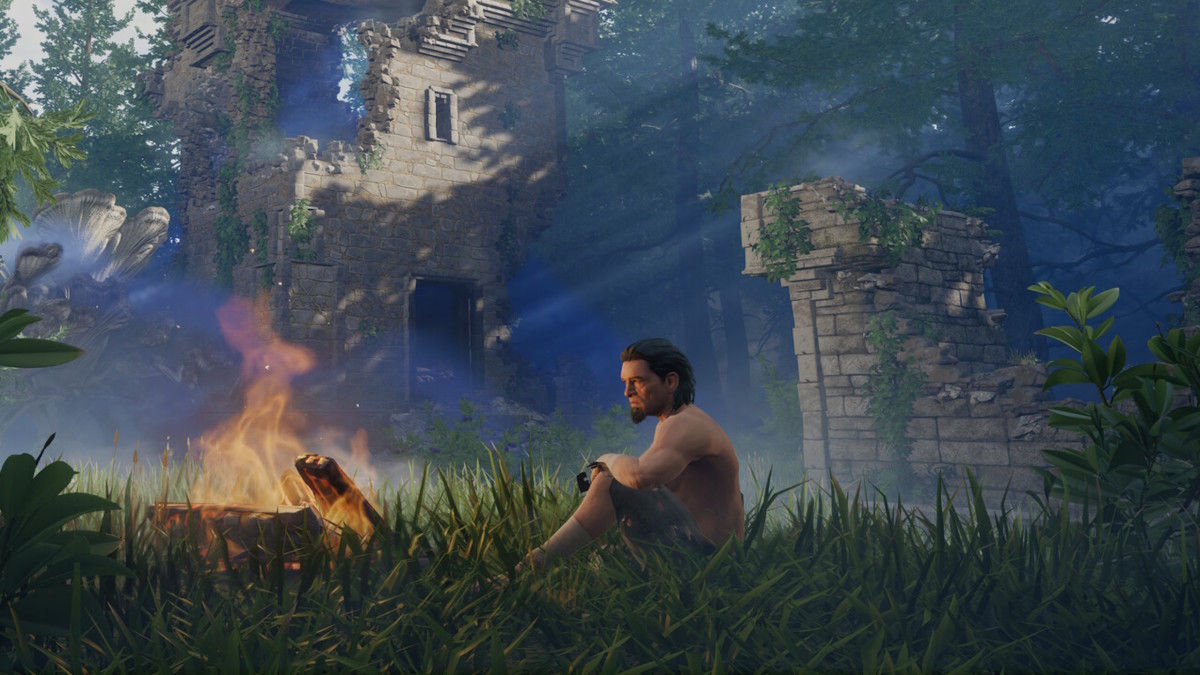 A man in shabby clothes is sitting next to a campfire in the middle of stone ruins
