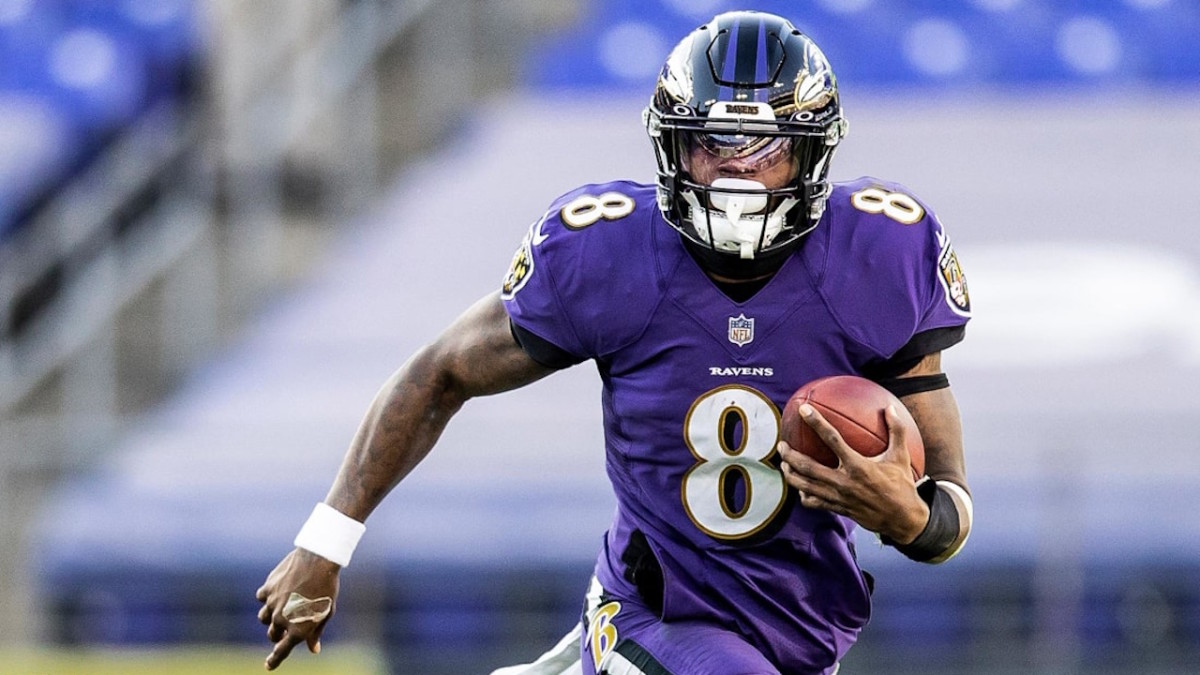 Lamar Jackson, a Black man wearing a black NFL helmet and purple jersey, is running down a football field while holding a ball in his left hand