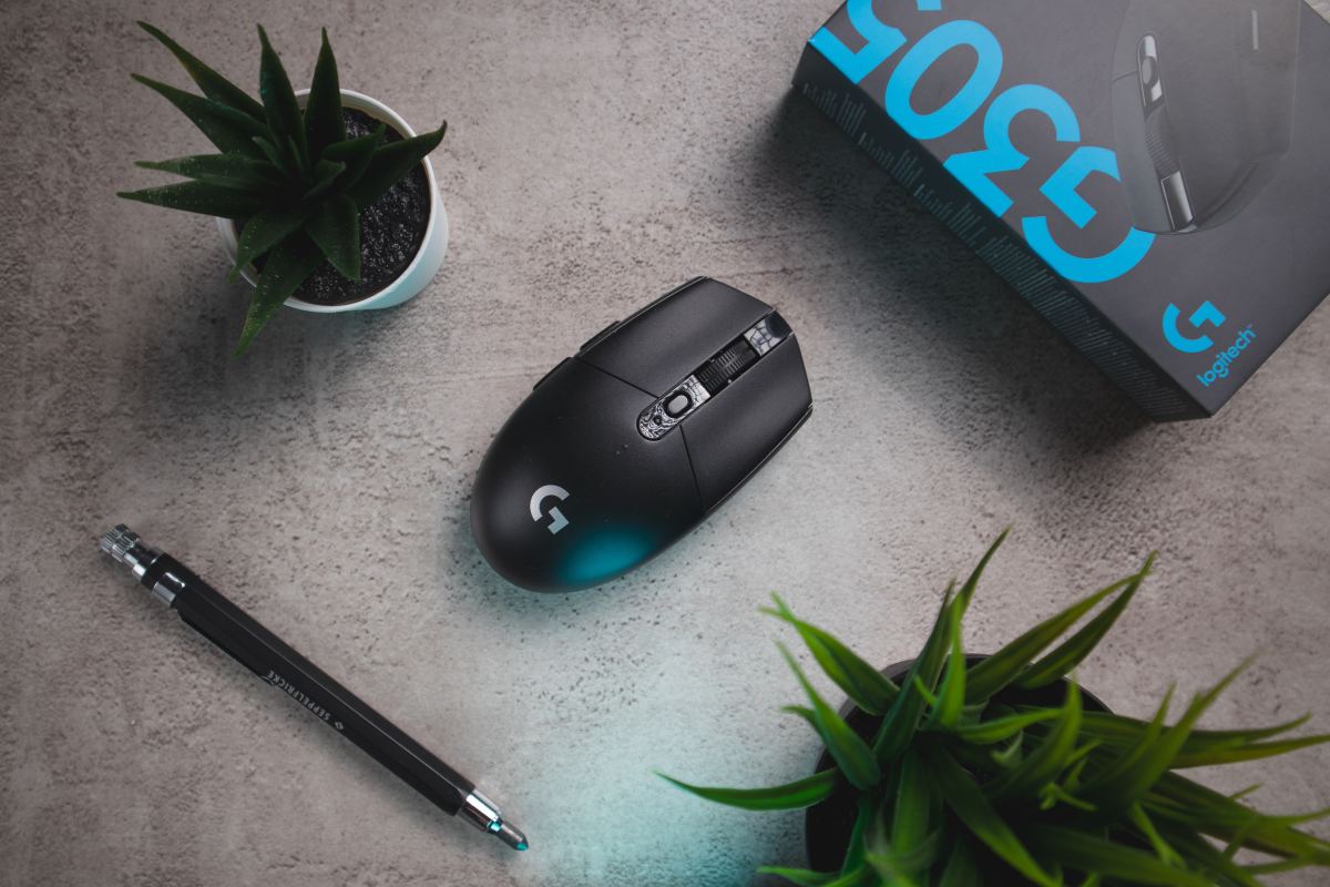 Photo of the Logitech G305 mouse shown next to its box, a pen and two succulents.
