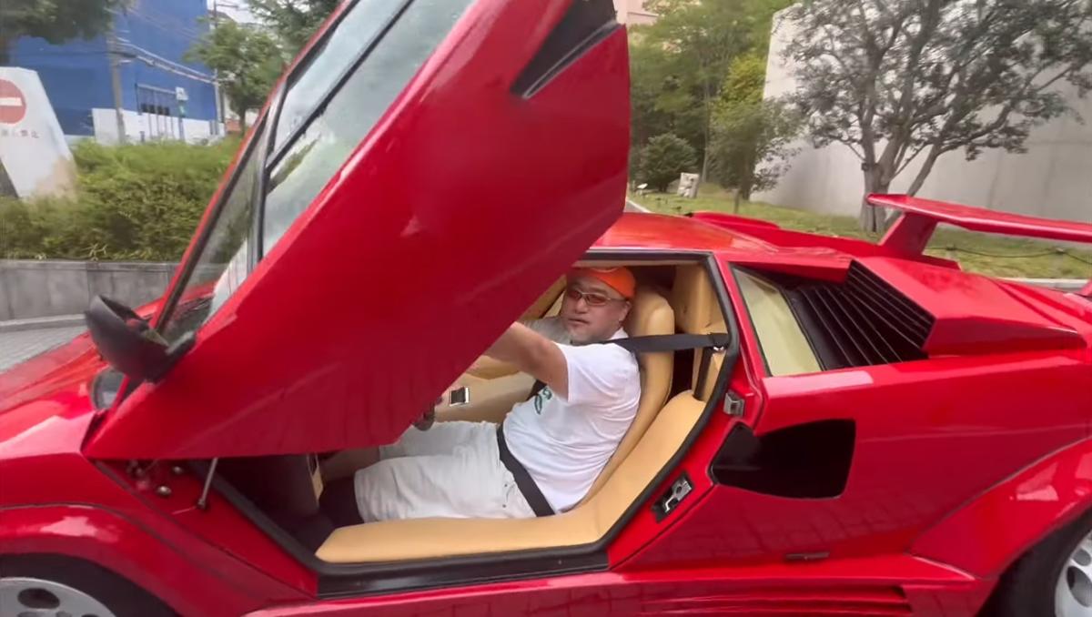 Hideki Kamiya sitting in his red Lamborghini Countach.